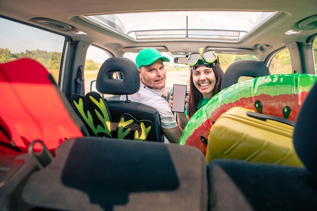 Sonriente pareja feliz en coche sosteniendo teléfono con pantalla blanca