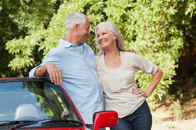 Sonriente pareja madura abrazando en su cabriolet rojo