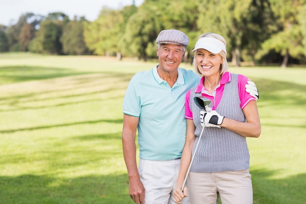 Sonriente pareja madura de pie en el campo de golf