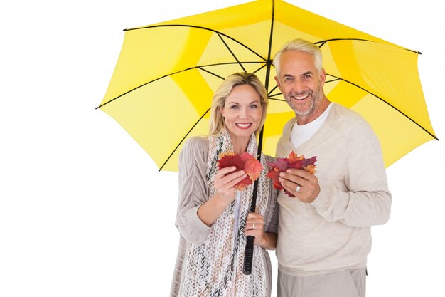 Sonriente pareja mostrando hojas de otoño bajo paraguas