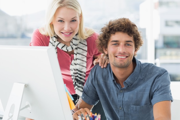 Sonriente pareja ocasional usando la computadora en la oficina brillante