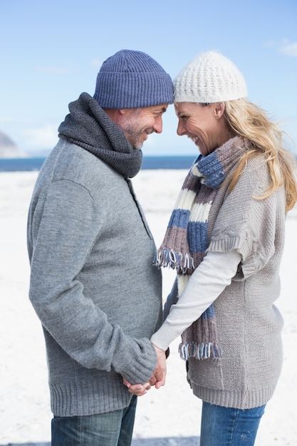 Sonriente pareja de pie en la playa con ropa de abrigo