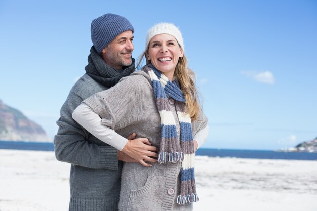 Sonriente pareja de pie en la playa con ropa de abrigo