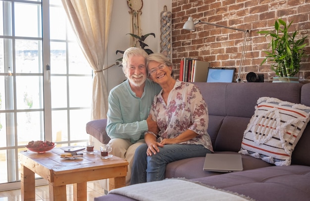 Sonriente pareja senior en casa sentado en el sofá mirando a la cámara. Pared de ladrillo en el fondo