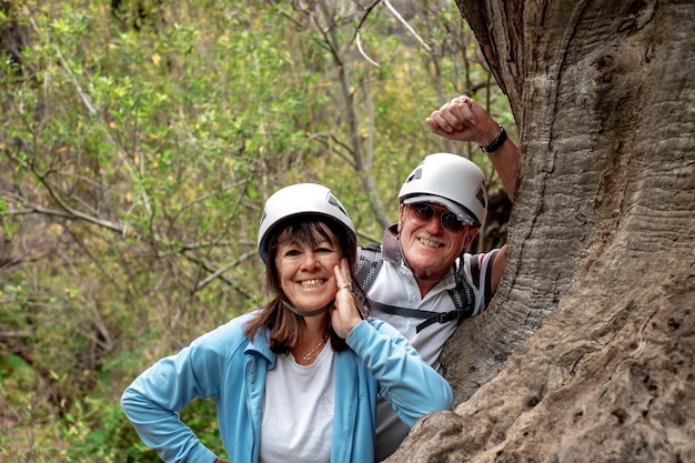 Sonriente pareja senior en el día de trekking de montaña descansando apoyado contra el tronco de un árbol