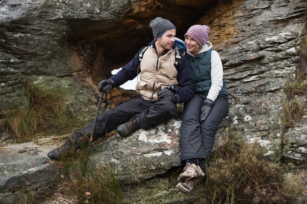 Sonriente pareja sentada en la roca durante una caminata