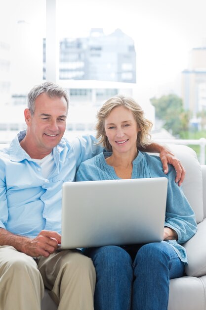 Sonriente pareja sentada en su sofá con la computadora portátil