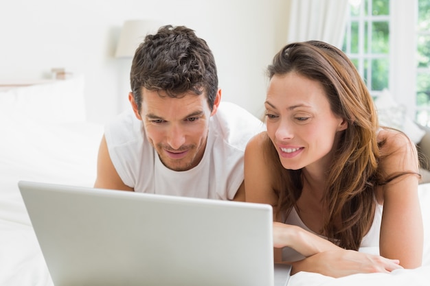 Sonriente pareja usando laptop en la cama