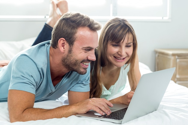 Sonriente pareja usando laptop mientras está acostado en la cama