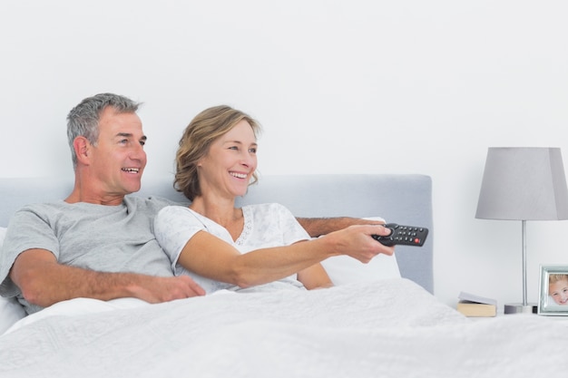 Sonriente pareja viendo la televisión en la cama