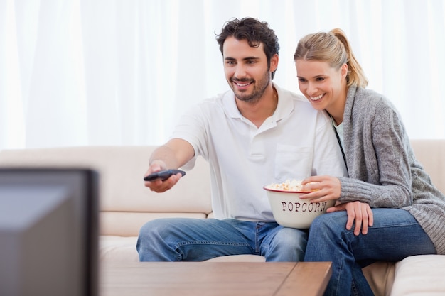 Sonriente pareja viendo la televisión mientras come palomitas de maíz