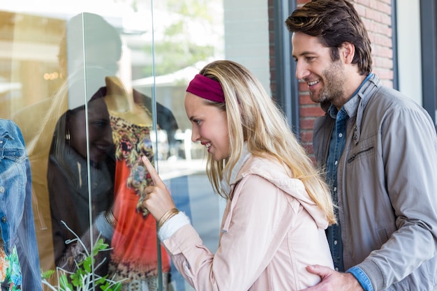 Foto sonriente pareja yendo de compras en la ventana y apuntando a la ropa