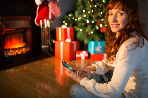 Sonriente pelirroja con smartphone en Navidad