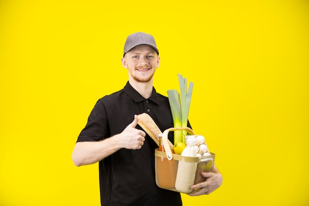 Sonriente repartidor sostiene la cesta con víveres mostrando como signo con el pulgar hacia arriba