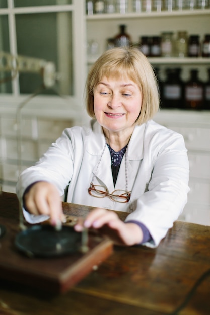 Sonriente rubia farmacéutica de mediana edad trabajando con escalas vintage en la farmacia