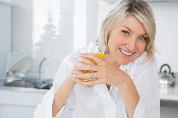 Sonriente rubia con jugo de naranja en la cocina