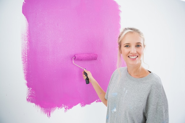 Sonriente rubia pintando su pared rosa