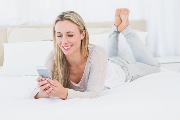 Sonriente rubia con smartphone en la cama