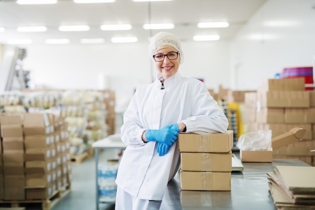 Sonriente trabajadora apoyándose en cajas. Almacén interior.