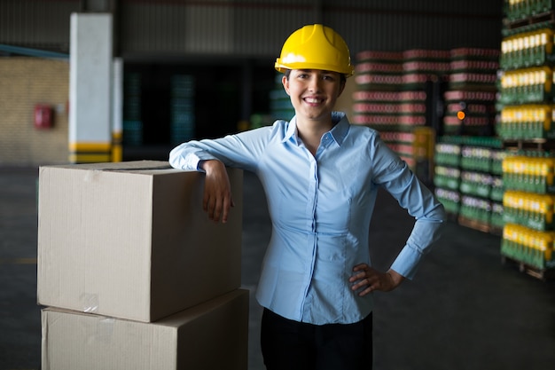 Sonriente trabajadora de fábrica de pie con la mano en la cadera en fábrica