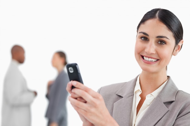 Sonriente vendedora sosteniendo teléfono celular con colegas detrás de ella