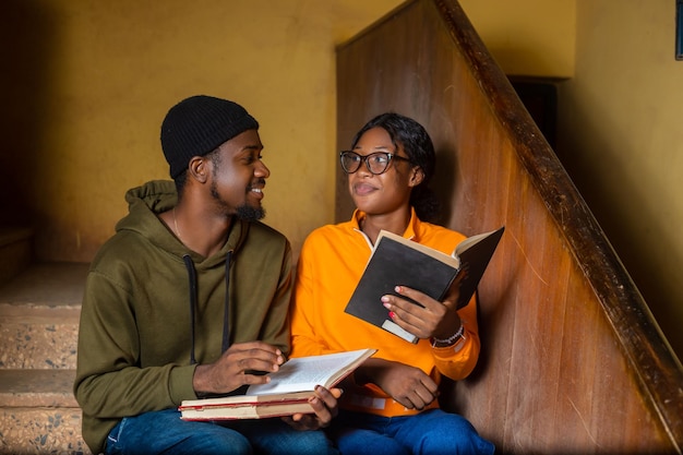 Sonrientes amigos estudiantes universitarios masculinos y femeninos africanos discutiendo sobre sus libros