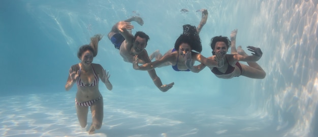 Sonrientes amigos mirando la cámara bajo el agua en la piscina