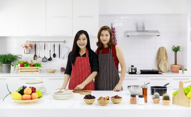 Sonrientes mujeres étnicas en delantales que sirven frutas maduras frescas en la mesa de la cocina.