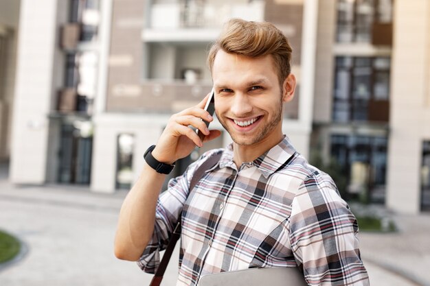 Sonrisa amistosa. Hombre joven alegre que le sonríe mientras tiene una conversación telefónica