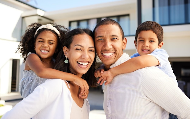 Sonrisa de amor y retrato de una familia feliz en el patio trasero de su casa moderna con un paseo a cuestas. Felicidad, padres e hijos, uniendo juegos y tiempo de calidad juntos al aire libre en la casa.