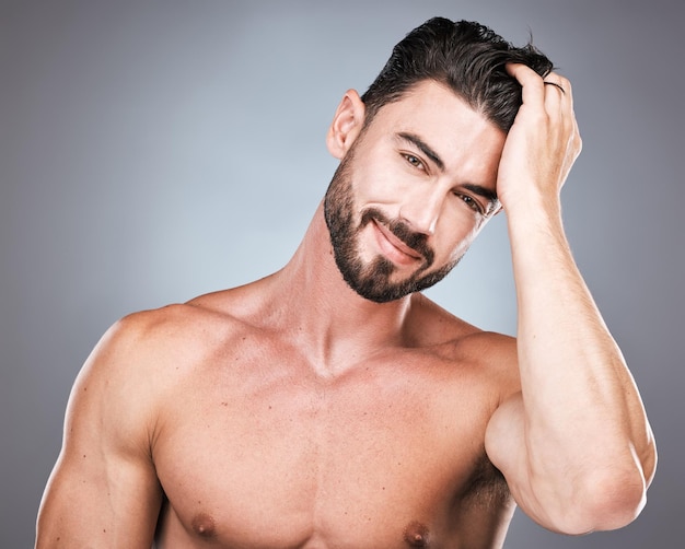 Foto sonrisa de belleza y retrato de hombre con la mano en el cabello mantenimiento de barba sexy y cuidado de la piel saludable fitness salud y spa cuidado facial modelo masculino con músculo en estudio aislado sobre fondo gris