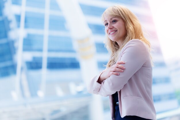 sonrisa caucásica inteligente y confidente de la empresaria y de pie con la construcción de la ciudad