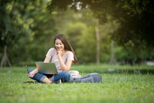 Sonrisa confiada mujer bastante joven que se sienta en lugar de trabajo en al aire libre con la computadora portátil. Concepto de trabajo