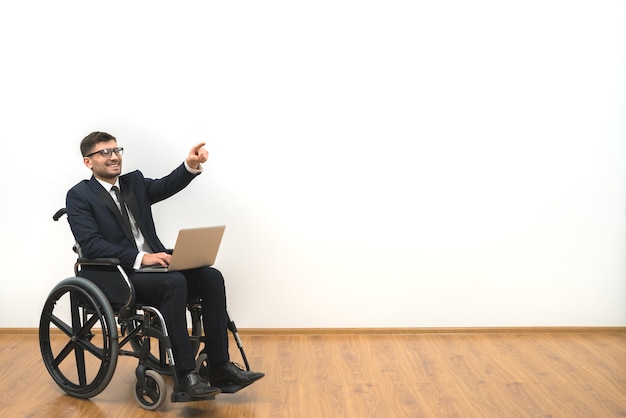 La sonrisa discapacitada con un portátil haciendo un gesto sobre la pared blanca de fondo