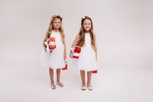 Sonrisa de dos niñas en vestidos blancos con regalos de Navidad sobre un fondo blanco