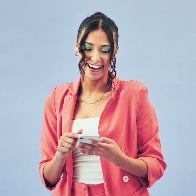 Sonrisa escribiendo y mujer con una conexión de teléfono inteligente y redes sociales en un fondo de estudio azul Modelo de persona o niña con un usuario de teléfono celular y búsqueda en Internet con maquillaje de belleza y aplicación