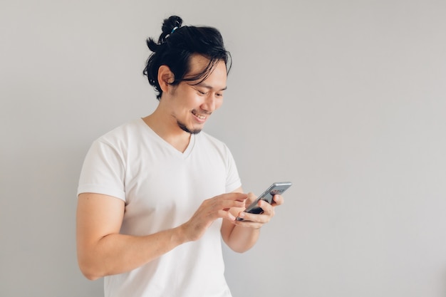 Sonrisa y feliz hombre de pelo largo en camiseta blanca casual está usando smartphone.