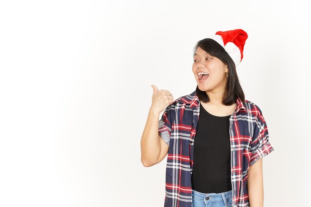 Sonrisa feliz que señala el producto a la izquierda de la mujer asiática con camisa a cuadros roja y gorro de Papá Noel