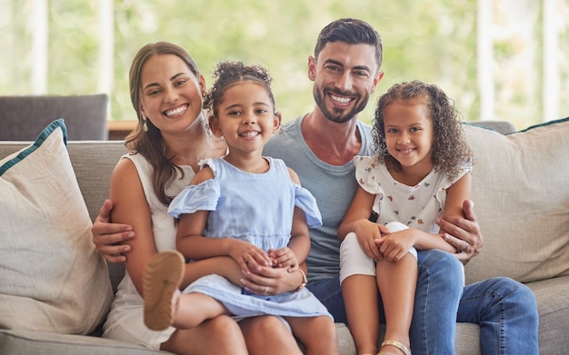 Sonrisa feliz y retrato de un vínculo familiar en la sala de estar para relajarse juntos en el sofá Cuidado de la felicidad y padres sentados y sosteniendo a sus hijas con amor en un sofá en casa