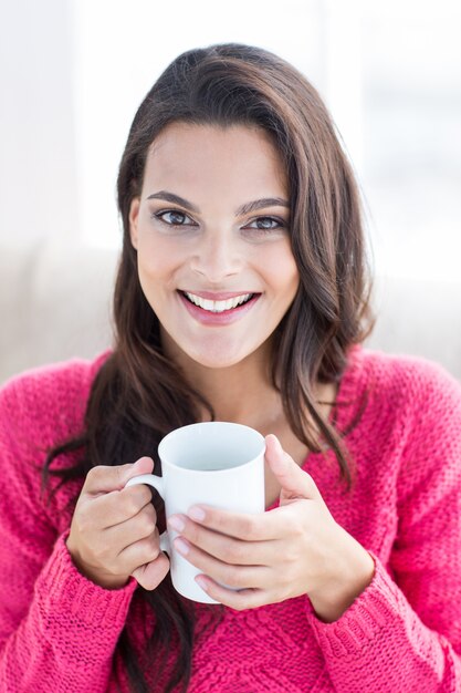 Sonrisa hermosa morena relajándose en el sofá y sosteniendo la taza