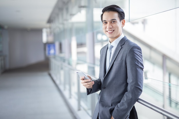 Sonrisa del hombre de negocios asiático joven que sostiene el teléfono inteligente en el concepto de negocio inteligente del área de la oficina
