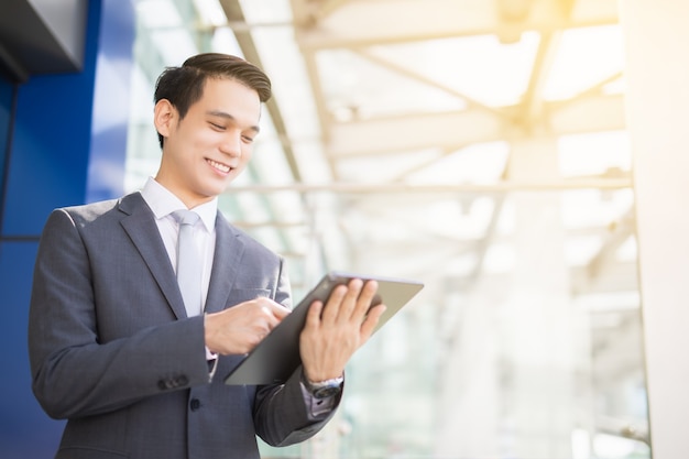 Sonrisa de hombre de negocios asiático y de pie en la oficina principal durante el uso de un stock de verificación de computadora portátil