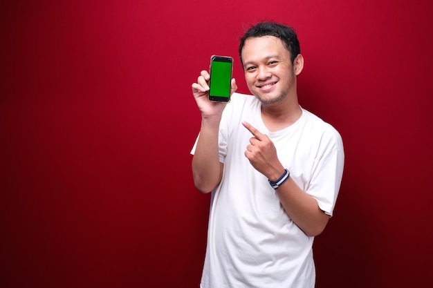 Sonrisa Joven asiático apuntando al espacio en blanco verde en el teléfono inteligente con fondo rojo