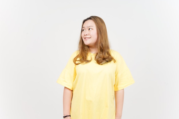 Sonrisa y mirando hacia otro lado de la hermosa mujer asiática con camiseta amarilla aislada en el fondo blanco