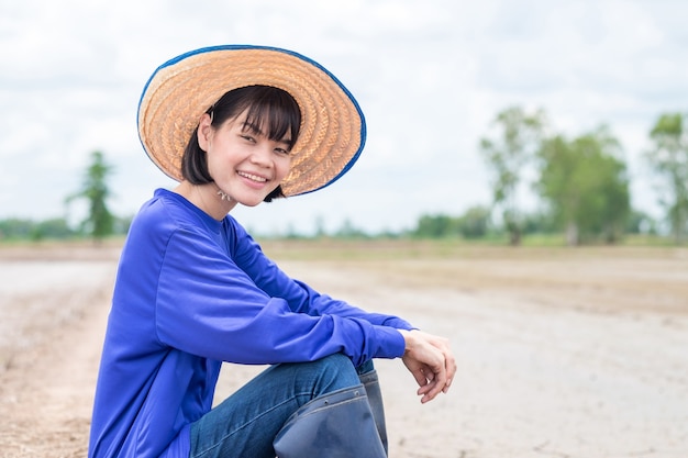 Sonrisa mujer agricultor asiático usar camiseta azul sentado en la granja de arroz