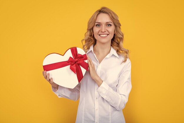 Sonrisa de mujer con caja de corazón presente sobre fondo amarillo