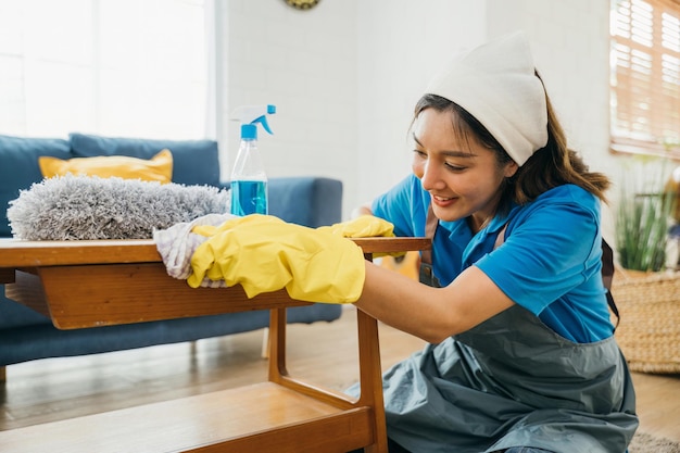 Foto con una sonrisa, una mujer diligente con guantes amarillos limpia y limpia su mesa de la sala de estar. su compromiso con la limpieza y la higiene del hogar es evidente en sus tareas de limpieza de rutina.