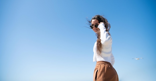 Sonrisa de mujer feliz mirando a través de gafas de sol en el cielo soleado para copiar el espacio, niña.