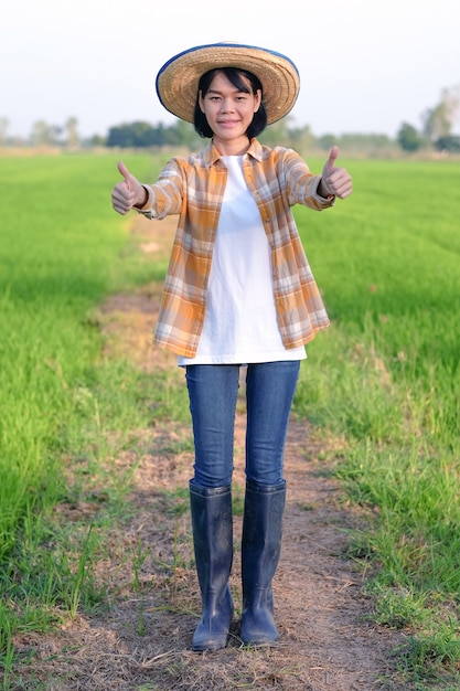 Sonrisa de mujer de granjero asiático y pulgar hacia arriba en la granja de arroz verde.