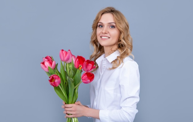 Sonrisa de mujer joven con ramo de tulipanes de primavera sobre fondo gris